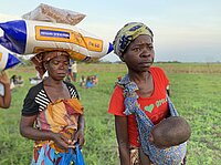 Antonia Algurau (22) mit ihrem Baby undnd Shiga Sharga (links) bei der Verteilung von Lebensmitteln in den Dörfern des Distrikts Nhamatanda. Jede Familie erhält 25kg Mais, 1kg Salz, 1kg Zucker, 1l Sojaöl, 5kg Bohnen, 2 Pakete Seife. Der Zykon Idai hat im März 2019 weite Teile des Nordens von Mosambik zerstört. Durch anschließende Regenfälle sind weite Gebiete überschwemmt. Die Menschen sind dringend auf Nothilfe angewiesen. Die Diakonie Katastrophenhilfe arbeitet vor Ort mit der langjährigen Partnerorganisation CEDES (Comité Ecuménico para o Desenvolvimento Social) zusammen. Copyright: Elisa Iannacone/Diakonie Katastrophenhilfe